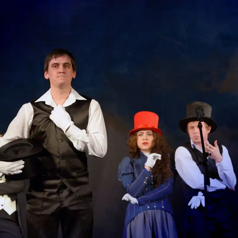 Actors in tuxedos and hats on stage.
