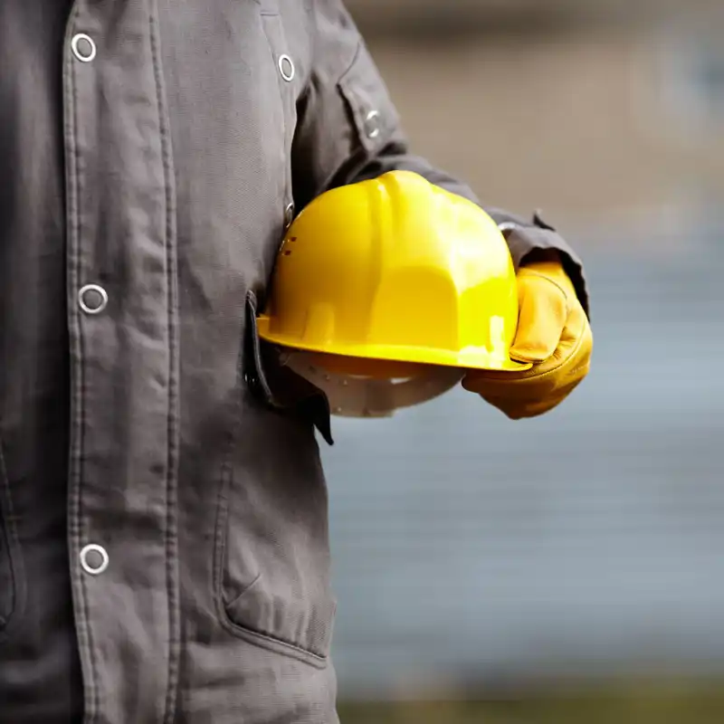 Closeup of a construction worker holding a yellow helmet.