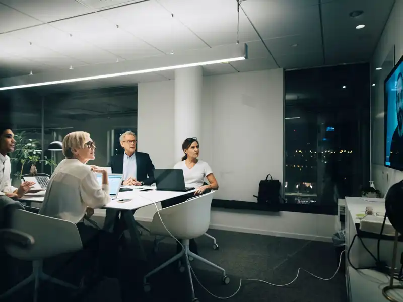 Colleagues looking at businessman during video conference meeting at night in office