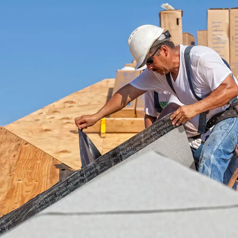 Roofer tears off protective cover of underlayment on a new roof.