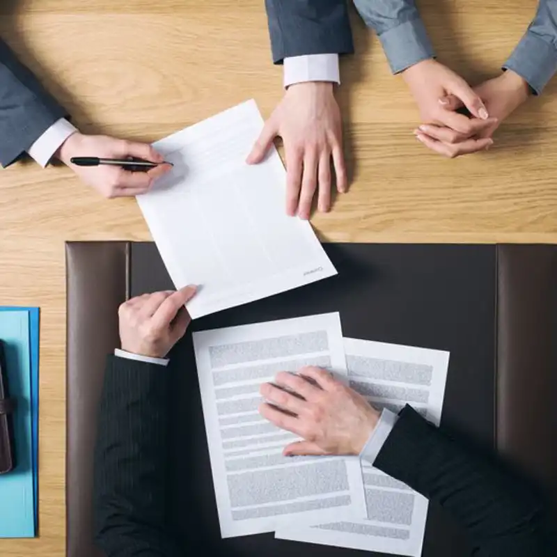 Business man and woman sitting at the lawyers's desk and signing important documents.