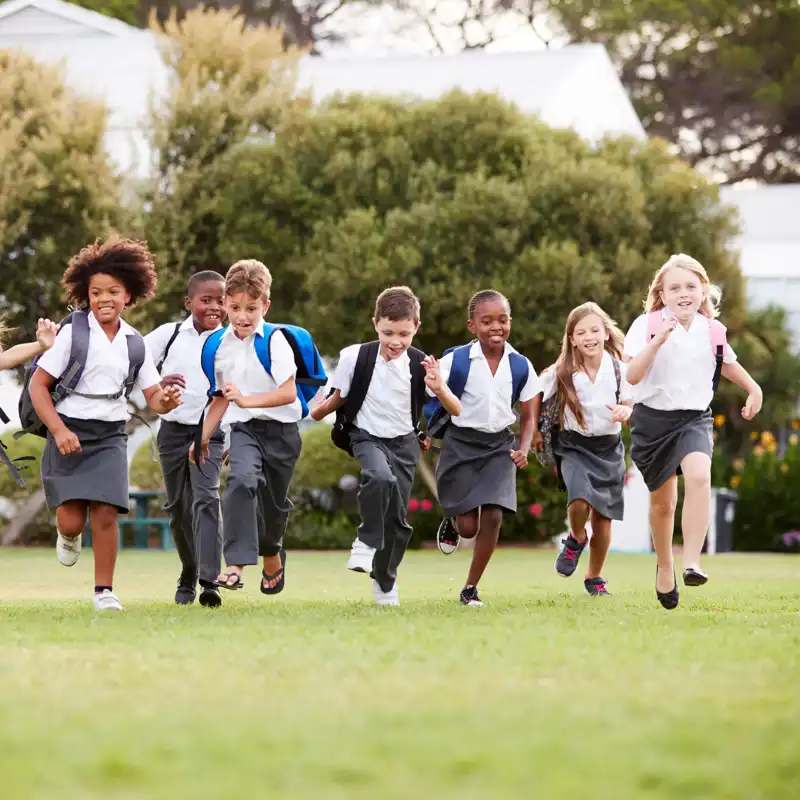 Excited elementary school children wearing uniforms running across the field at recess.