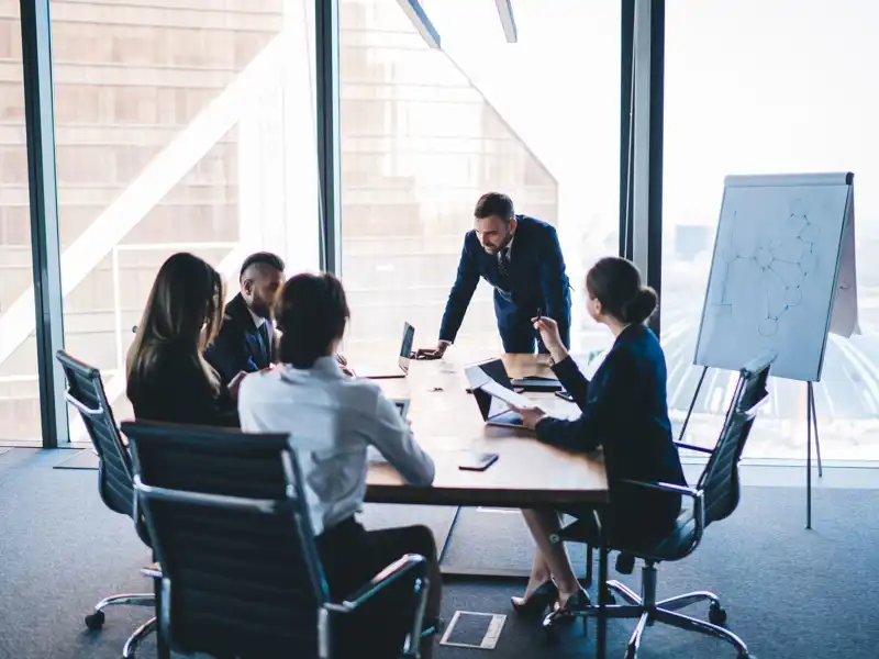 Group of coworkers in formal wear sitting at table in conference room and arguing about project of company development during meeting