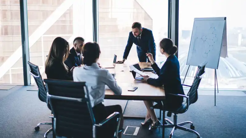 Group of coworkers in formal wear sitting at table in conference room and arguing about project of company development during meeting