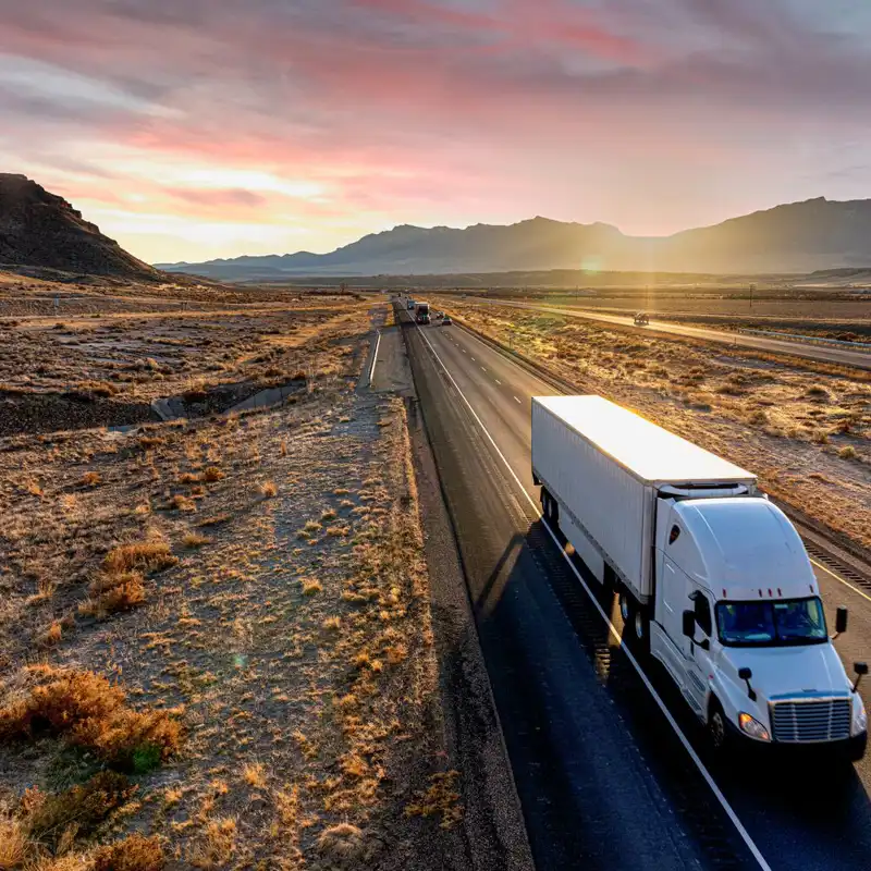 White semi-trailer truck heading down a four-lane highway at dusk.