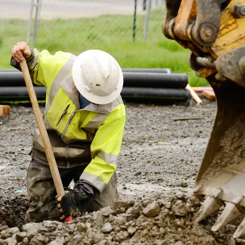 Worker using a small-tracked excavator to dig a hole to fix a water leak.