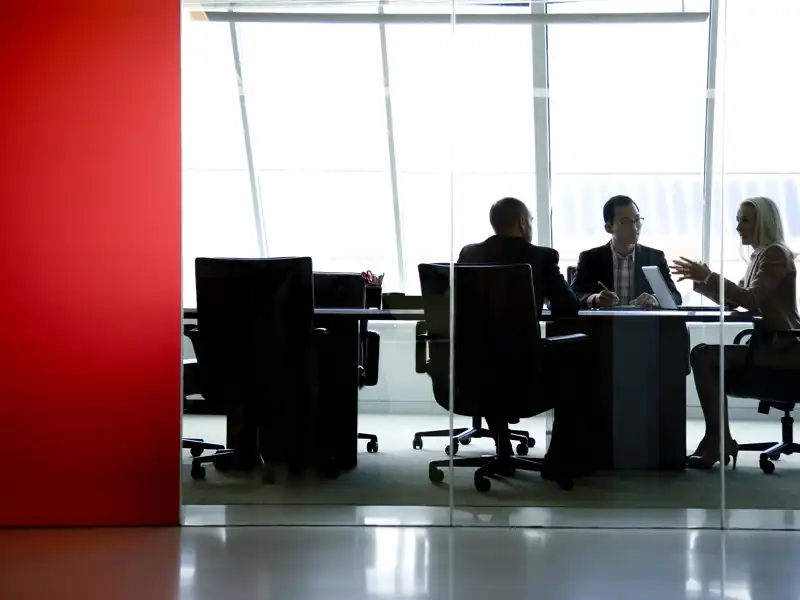 Coworkers having a meeting in a glass wall conference room.
