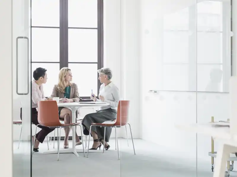 Three people sitting a table in a bright room.