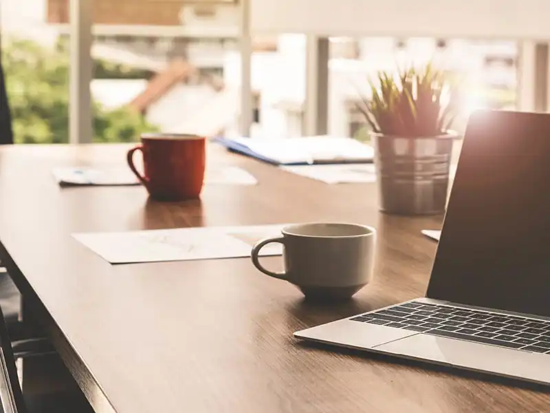 Laptop left open on top of a desk with two cups.