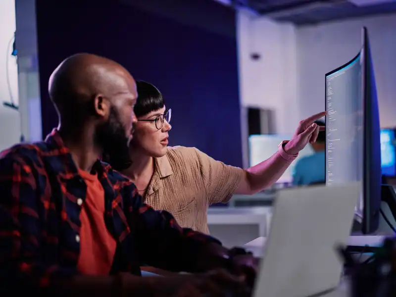 Two people in casual dress study data on a computer monitor.