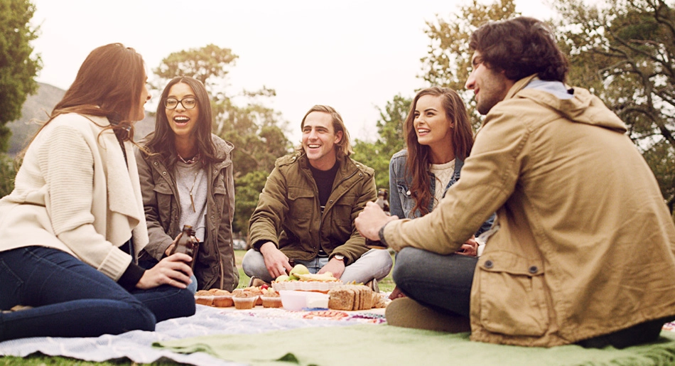 Five people sitting on the ground outdoors having a picnic.