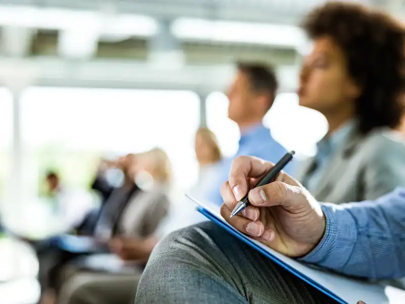 close up of a man holding a pen and notebook at a business conference