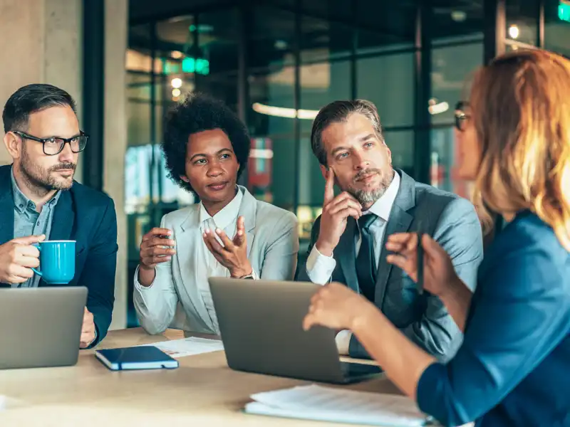 Group of diverse coworkers having a discussion while using their laptops.