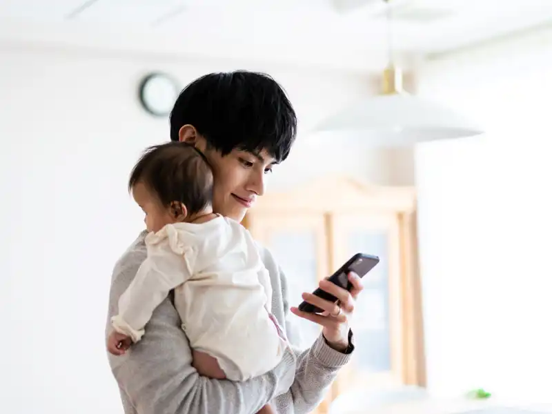 Father holding baby looking at his phone.