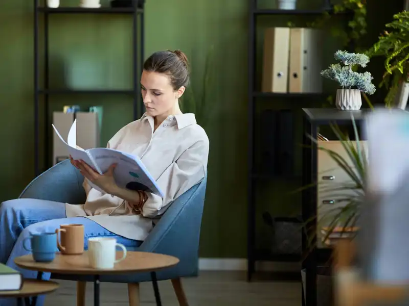 Woman sitting in a chair in a modern waiting room reading a magazine.