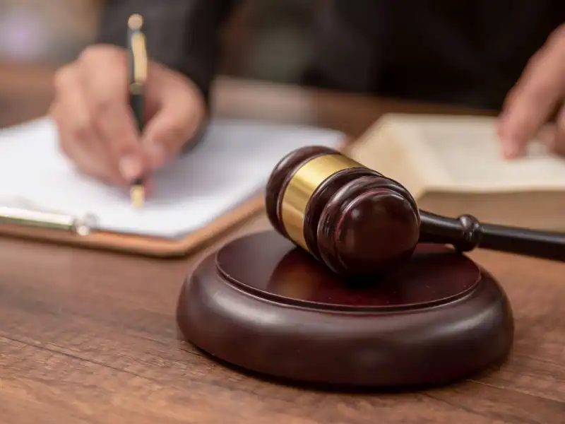 Close up of a gavel on a desk with a judge writing in the background.