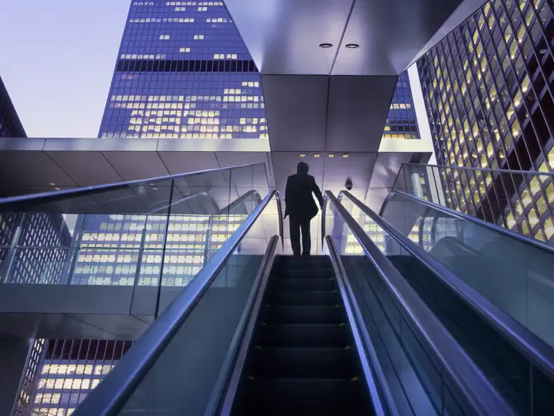 Businessman walking up an escalator at sunrise.