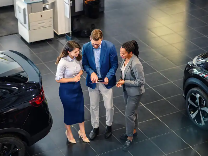 A woman and a man holding a tablet, engaged in a discussion about an auto loan at a car dealership.