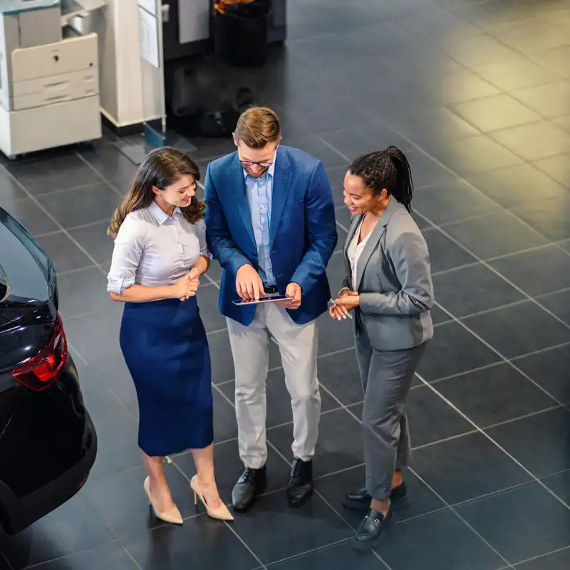 A woman and a man holding a tablet, engaged in a discussion about an auto loan at a car dealership.