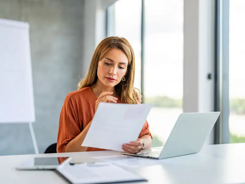 A woman seated at a desk, working on a laptop surrounded by papers.