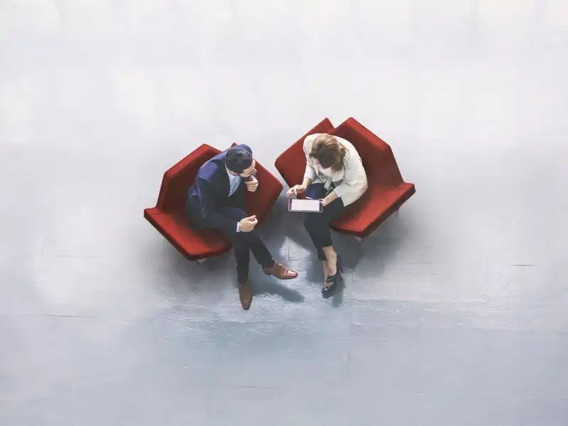 People have a discussion from two stylish red chairs in a stark room