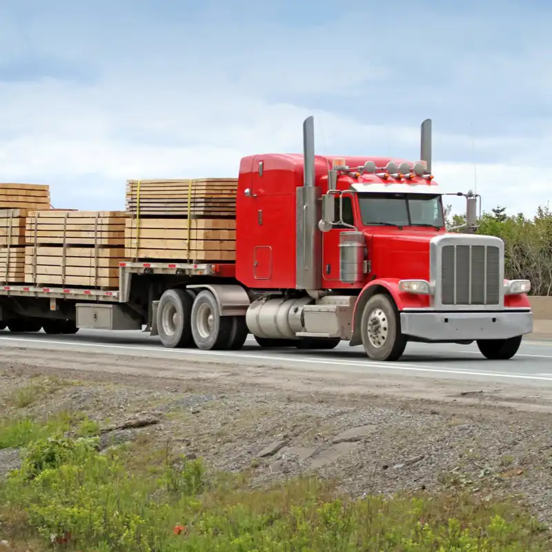 Red semitruck driving down the highway carrying lumber.