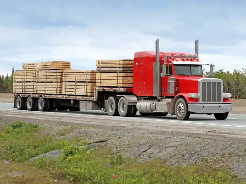 Red semitruck driving down the highway carrying lumber.
