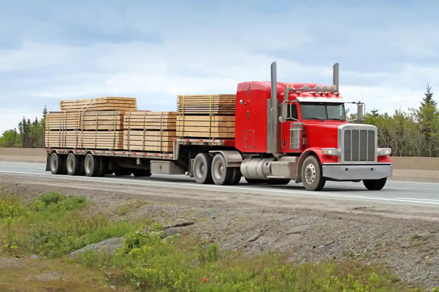 Red semitruck driving down the highway carrying lumber.