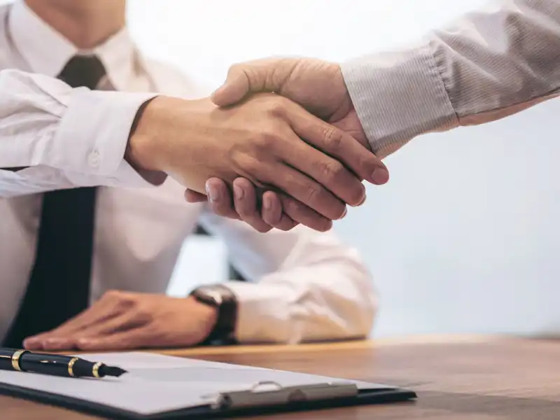 Agent and customer shaking hands after signing contract documents for realty purchase.