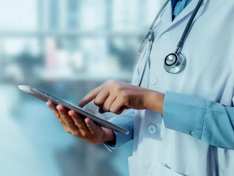 Medical professional wearing a stethascope and using a tablet.