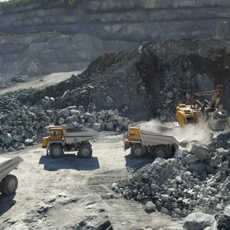 Excavator and heavy mining dump trucks in a limestone quarry.