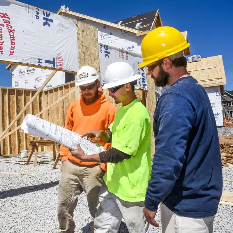 Three male construction workers, carpenters, wearing hardhats looking at blueprints.